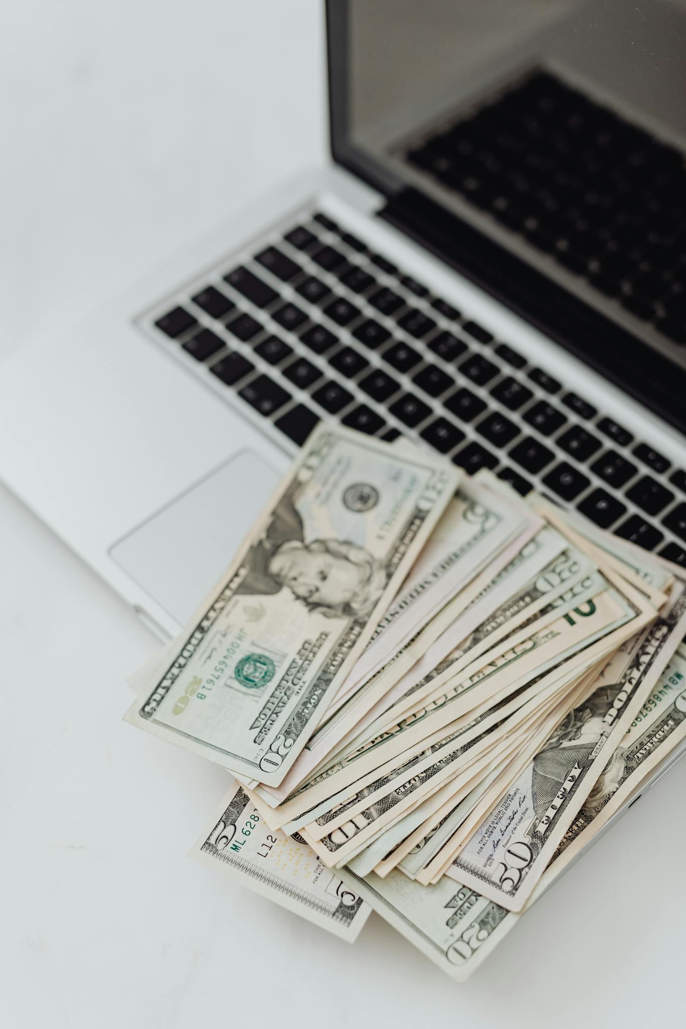 Stack of US dollar bills on a laptop keyboard representing online finance and budgeting.